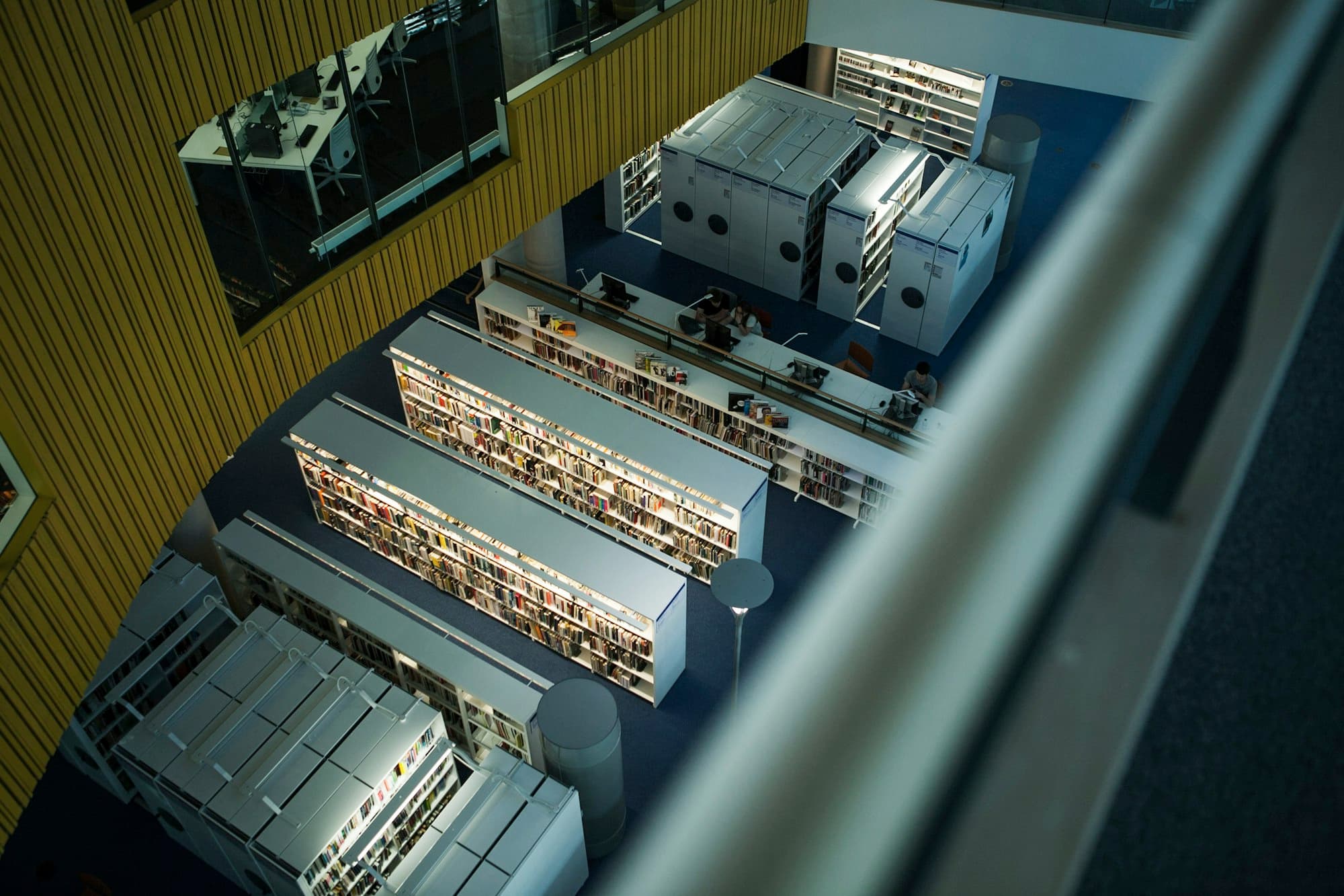 Library stacks seen from a balcony above, rows of shelving on a blue floor